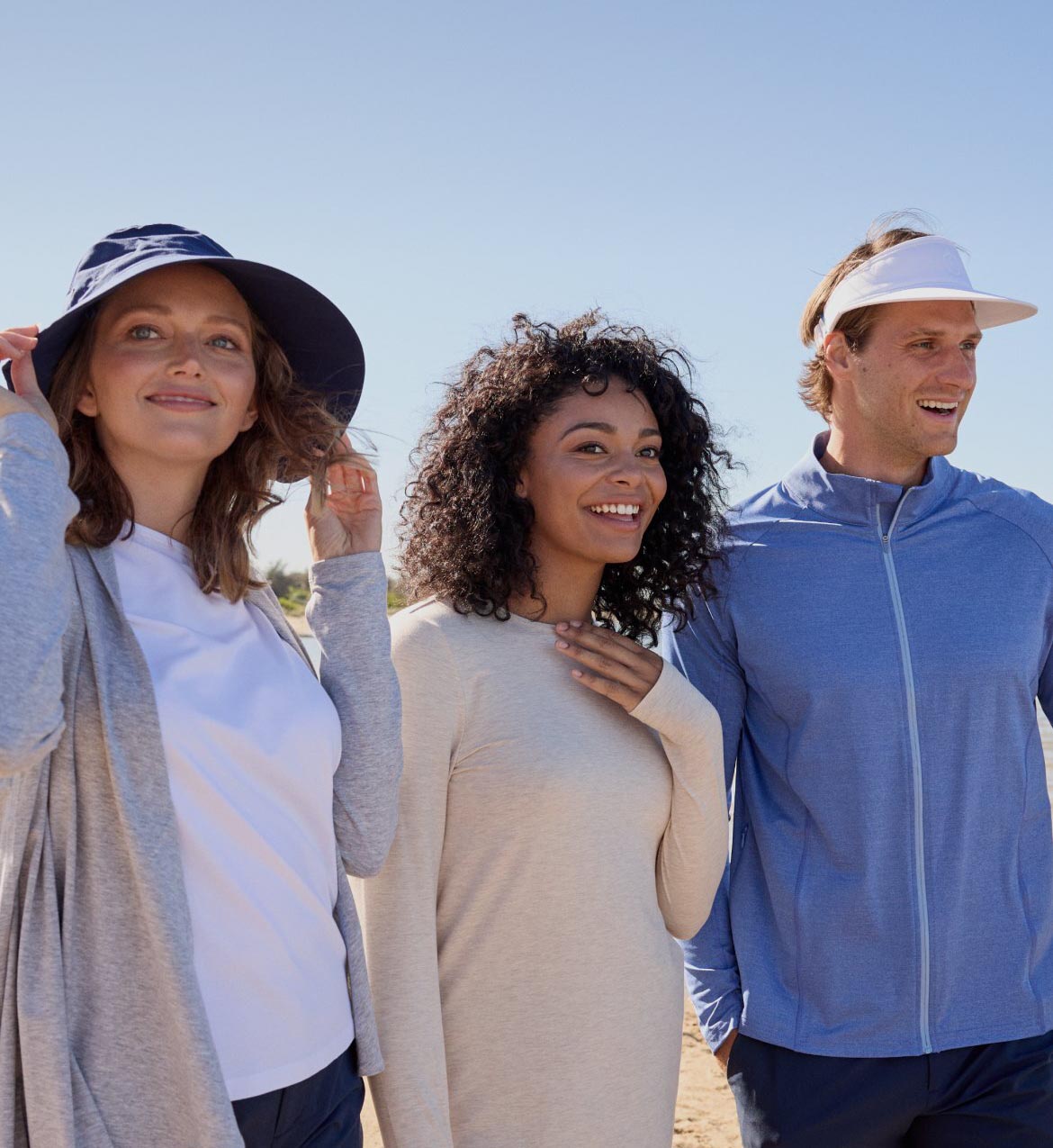 Three people standing together outdoors wearing sun protective clothing and hats.