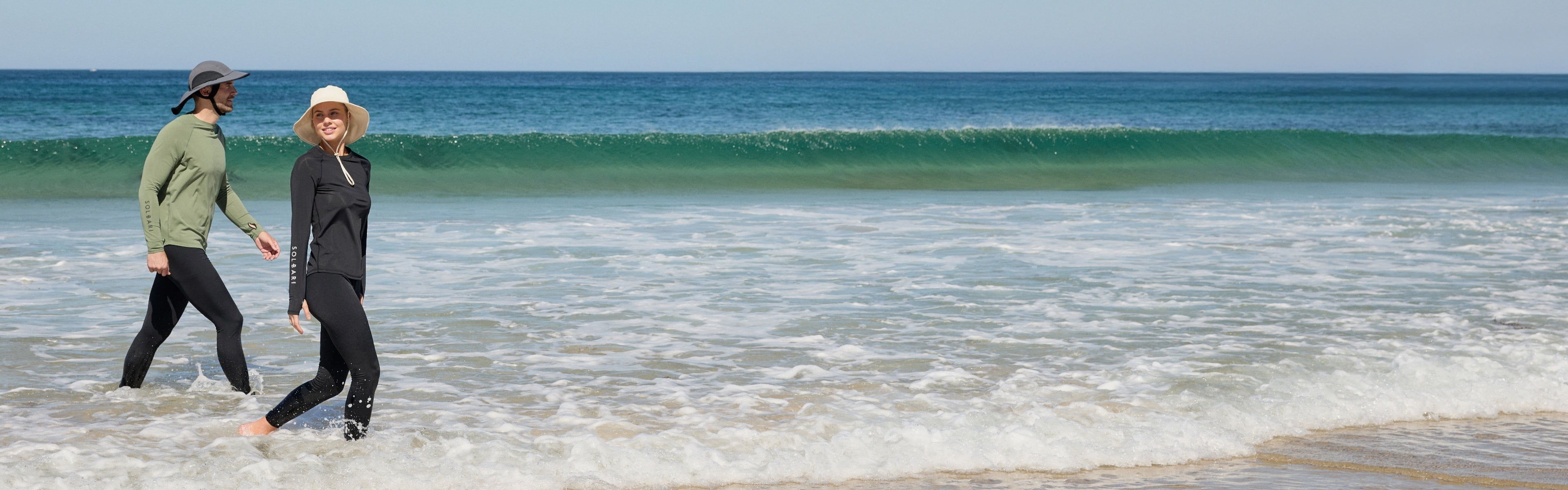 Man and woman waking in the sea wearing Solbari hats